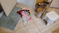 Multiple items including bath mat, trash bins, stools, towels, and bath wrap laid out on tiled floor