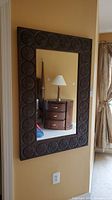 Full view of the rectangular wall mirror hung on a wall, showing the dark carved wood frame and mirrored glass reflecting a room interior.