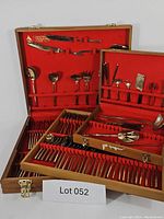 Full view of open wooden cases showing the large collection of vintage gold tone flatware organized by type and size, with knives, forks, spoons and specialty serving pieces visible.