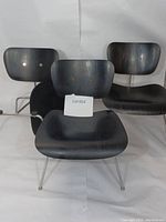 Three chairs viewed from front, black plywood seats and backs, chrome tubular legs