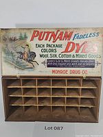 Full frontal view of the antique Putnam Fadeless Dyes wooden shop display with upper graphic panel and open compartments below.