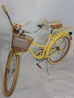 Full view of the yellow adult-sized Huffy cruiser bike featuring brown pedals, a padded beige and brown saddle, front basket, and rear rack.