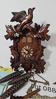 Front view of wooden cuckoo clock with carved birds, leaves, and pine cone weights