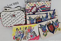 Lot with six Brighton bags showing front of various bags including white love script crossbody, a pouch with fashion illustration, large zippered bag with heart chains and ribbons, and two smaller matching pouches with bird and crowned heart design.