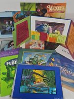 Photo showing multiple Disney lithographs stacked and displayed, including Toy Story, Monsters Inc., Mickey's Once Upon a Christmas, Sleeping Beauty, Flubber, and Little Mermaid prints.