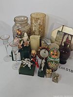 Overview of various home decor items including glass vase, glasses, candles, ornaments, and nesting dolls on a white surface