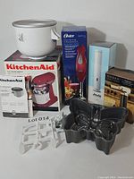 Full view of lot showing KitchenAid ice cream maker attachment with bowl, Oster hand blender in box, Joule sous vide in box, culinary torch, and Nordicware butterfly cake pan.