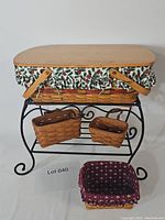 Full lot view: large rectangular basket with berry-pattern cotton liner on wrought iron stand with wood top, two small hanging baskets on lower shelf, maroon-lined basket in front
