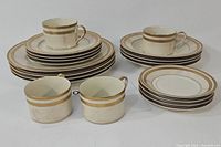 Full set of white ceramic Oscar de la Renta dishware stacked and arranged, showing gold band design.