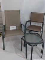 Photo showing two small chairs with beige mesh fabric seats and backs, and one larger chair with a higher back, all with black metal frames, plus one square glass-top table