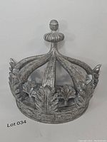 Front view of the decorative wall-mounted canopy crown showing the aged metal finish, leaf motifs, and rounded finial top.