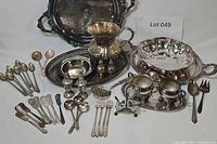 Full overview of the silver serving and tableware collection showing trays, pitcher, salt and pepper shakers, cream and sugar set, and a variety of silverware arranged on a white surface.