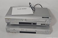 Two stacked VCR/DVD combo players, silver finish, visible logos and control buttons for both brands