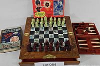 Full view of the chess board with carved floral border holding chess pieces in two colors. Chess board drawer open showing backgammon set with dice and pieces. Mystery Jig puzzle box placed to left side. Magic Designer kit box visible behind chess board.