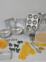 Photo showing full set of vintage children's Tupperware bowls with lids, metal baking pans and molds, yellow measuring cups and spoons, green animal-shaped cookie cutters, and small utensils including whisk and spatula.