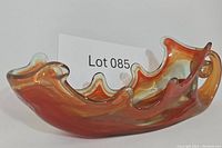 Side view of the swirled glass dish showing its curved ruffled edge and amber-red swirl pattern.