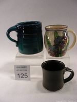 Set of three signed artist pottery mugs arranged showing various colors and shapes.