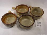 Four vintage soup bowls arranged together showing variation in glaze tones, handles, and sizes.