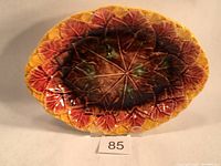 Full view of oval majolica platter showing colorful begonia leaf pattern in burgundy, yellow and brown tones with a glossy surface.