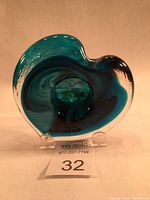 Front view of the blown glass heart sculpture showing the blue and turquoise swirls with clear edges and the lot number displayed below.