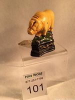 Side-angle photo showing the pig door stop on a transparent block, highlighting the yellow pig figure and sculpted base.
