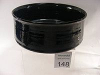 Black glossy glazed pottery baking dish shown from above, smooth and reflective surface, flared rim.