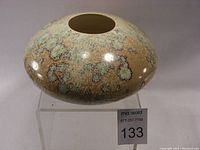 Front view of the rounded crystalline glaze porcelain vase on a clear stand showing surface glaze detail.