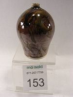 Front angled view of small porcelain vase with brown, green, and muted purple tomaku glaze showing glossy texture and glaze overlay.