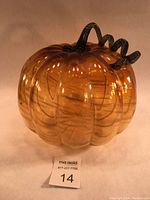 Front view of large amber-colored glass pumpkin showing ribbed pumpkin shape and dark smokey green curled stem.
