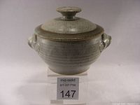 Front view of light-colored stoneware casserole dish with lid, showing rounded form and side handles.