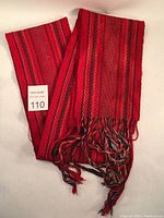Full view of folded red cotton sash with fringed ends showing mixed red, blue, and green threads, highlighting length and condition.