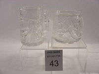 Front view of two clear glass mugs featuring embossed character designs from Batman Forever, Riddler and Robin