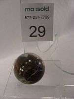 Glass paperweight displayed on clear stand, showing dark internal colors with reflective highlights