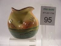 Angled front view showing vase shape, motto text, ship and sunset design, and chipped rim detail.