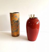 Two mid century ceramic vases on white surface: one red urn-shaped Scheurich, one tall textured orange/grey Royal Haeger.