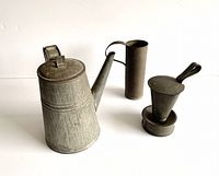 Three pieces of antique tin ware displayed together showing the coffee pot, the multi-functional container with lid and handle, and the measuring cup.