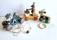 Photo of all three pull toys side by side: the elephant with metal bells and hoop, the rabbit playing a xylophone on yellow platform with red wheels, and the cow with a pull ring.