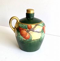 Side view of antique Limoges ewer showing gold handle and fruit branch motif on dark green background.