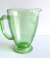 Front view of green depression glass water pitcher showing embossed floral design and shape.