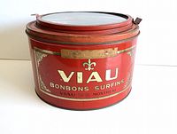 Front view of red round tin with glass lid showing Viau Bonbons Surfins branding and faded paper label.