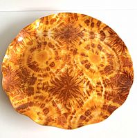 Top view of a round colorful Fab tray with ruffled edges and tie-dye pattern in yellow, orange and brown hues.