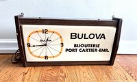 Front view of the rectangular Bulova advertising clock showing faux woodgrain frame, wood side panels, and clock face with 'Bulova' and 'BIJOUTERIE PORT CARTIER-ENR.' text