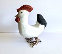 Side view of vintage carved wooden rooster showing white body, red comb and wattles, and black tail