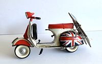 Side view showing red and white Vespa model with black tires, Union Jack on rear hub flare, and two brown surfboards attached.