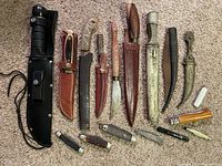 All 17 knives laid out showing a variety of pocket knives and fixed blade knives with leather sheaths on carpeted floor