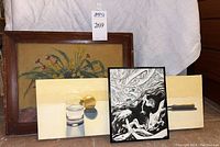 Three pieces of artwork: floral painting in wooden frame, minimalist still life painting of glass and lemon, black and white fantasy ink drawing framed in black metal.