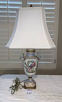 Full view of porcelain urn lamp with white shade and electrical cord visible on table.