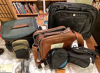 Various camera carrying bags including black backpack, brown leather crossbody, black and green pouches