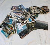 Large scattered collection of postcards on fabric surface showing various sizes and images including cityscapes and cultural scenes.