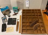 Photo showing all items including miniatures shelf, calculators, cassette recorder, paperweight, pencil sharpener, ruler, notepad, and combs arranged on table.
